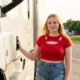 A confident woman truck driver standing in front of a Freightliner Cascadia semi-truck at a Tennessee truck stop