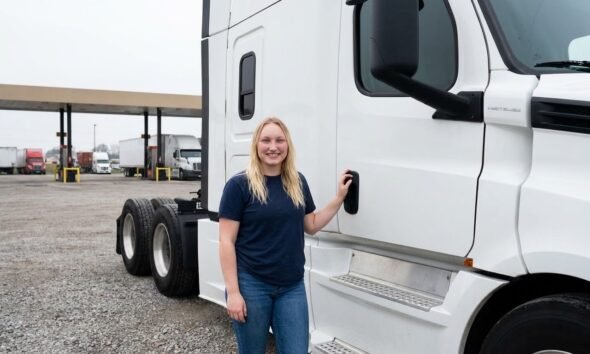 Female owner-operator standing beside bobtail semi-truck tractor without trailer at Columbus Ohio truck stop